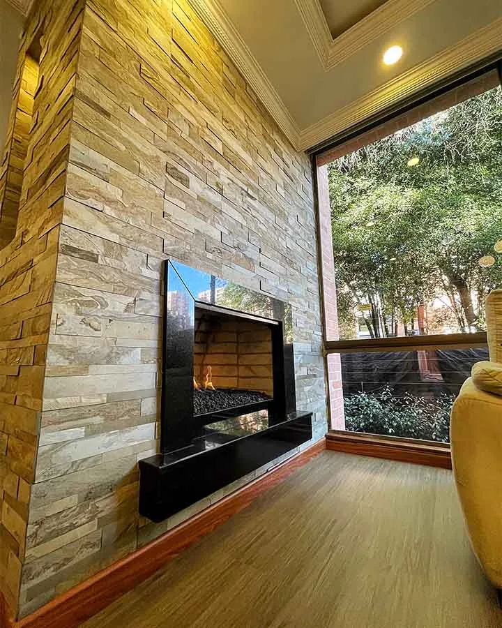 Chimenea decorada con piedra flexible 3D autoadhesiva StoneFlex Tan en sala residencial con ventanales.