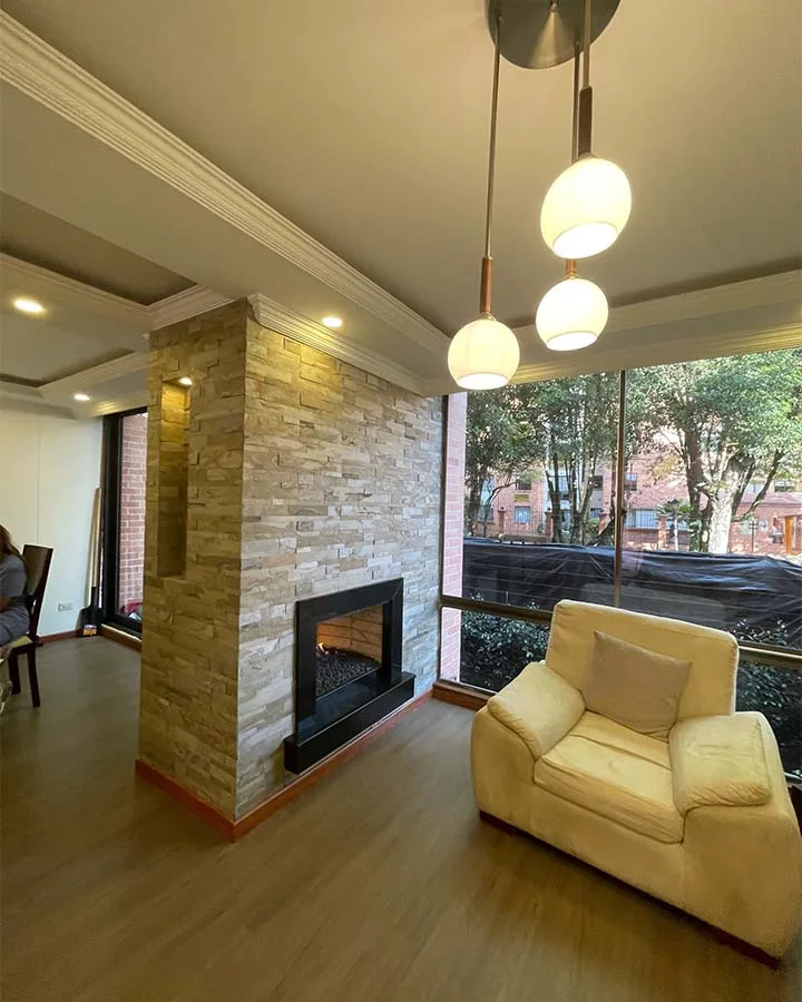 Chimenea decorada con piedra flexible 3D autoadhesiva StoneFlex Tan en sala residencial con ventanales.