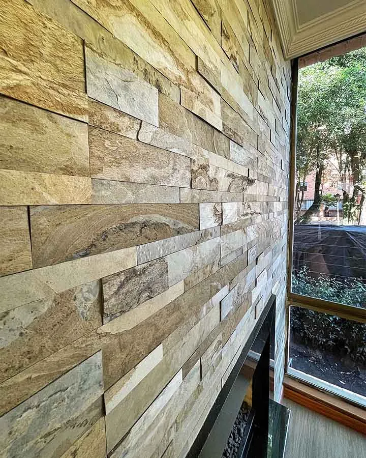 Chimenea decorada con piedra flexible 3D autoadhesiva StoneFlex Tan en sala residencial con ventanales.