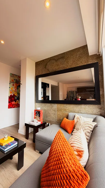 Revestimiento de pared con lámina de piedra flexible Silver Shine Gold de StoneFlex en una sala de estar, detrás de un sofá gris y un gran espejo rectangular negro.
