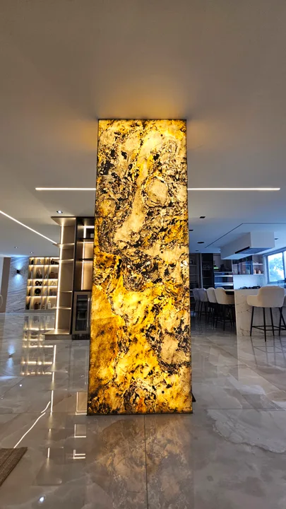 Columna arquitectónica retroiluminada revestida con lámina de piedra flexible translúcida de StoneFlex, destacando patrones naturales y vetas orgánicas oscuras en un interior moderno.