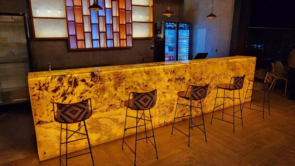 Barra de bar retroiluminada con panel frontal de piedra natural de ónix ámbar translúcido de StoneFlex, mostrando texturas orgánicas e iluminación cálida.